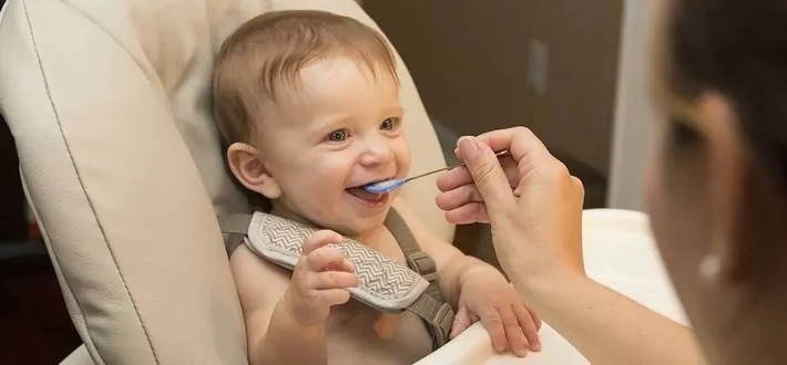 Smiling baby being fed with a spoon during a feeding and swallowing therapy session