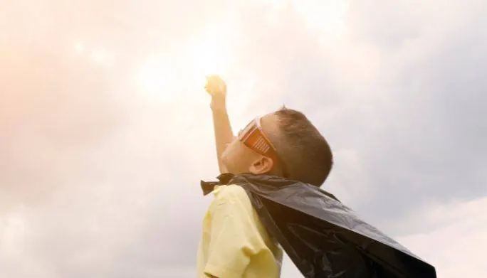 Young child in a superhero cape reaching toward the sky, representing growth and confidence supported by occupational therapy