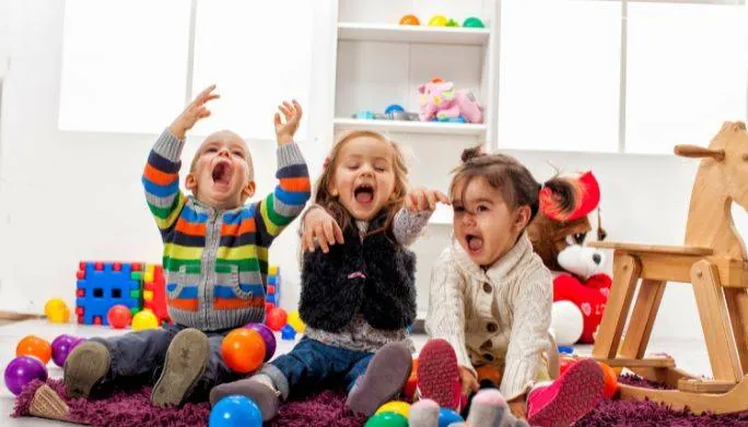 Group of young children laughing and playing together in a playroom