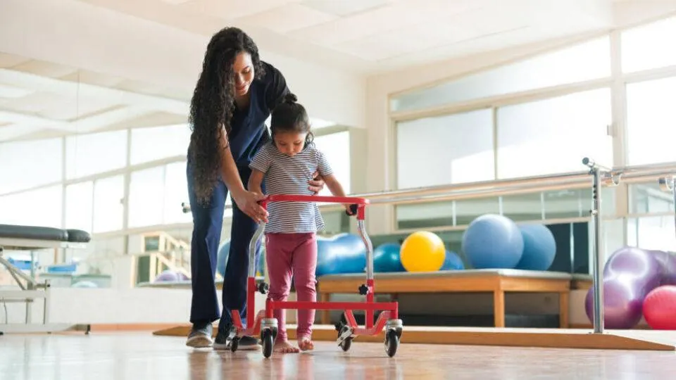Pediatric physical therapist helping a young child walk with a supportive walker