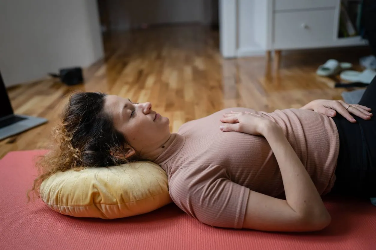 Woman resting on the floor with a hand on her abdomen during a pelvic floor recovery routine