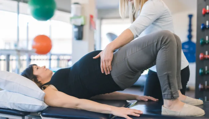 Physical therapist guiding a pregnant patient through a gentle movement exercise