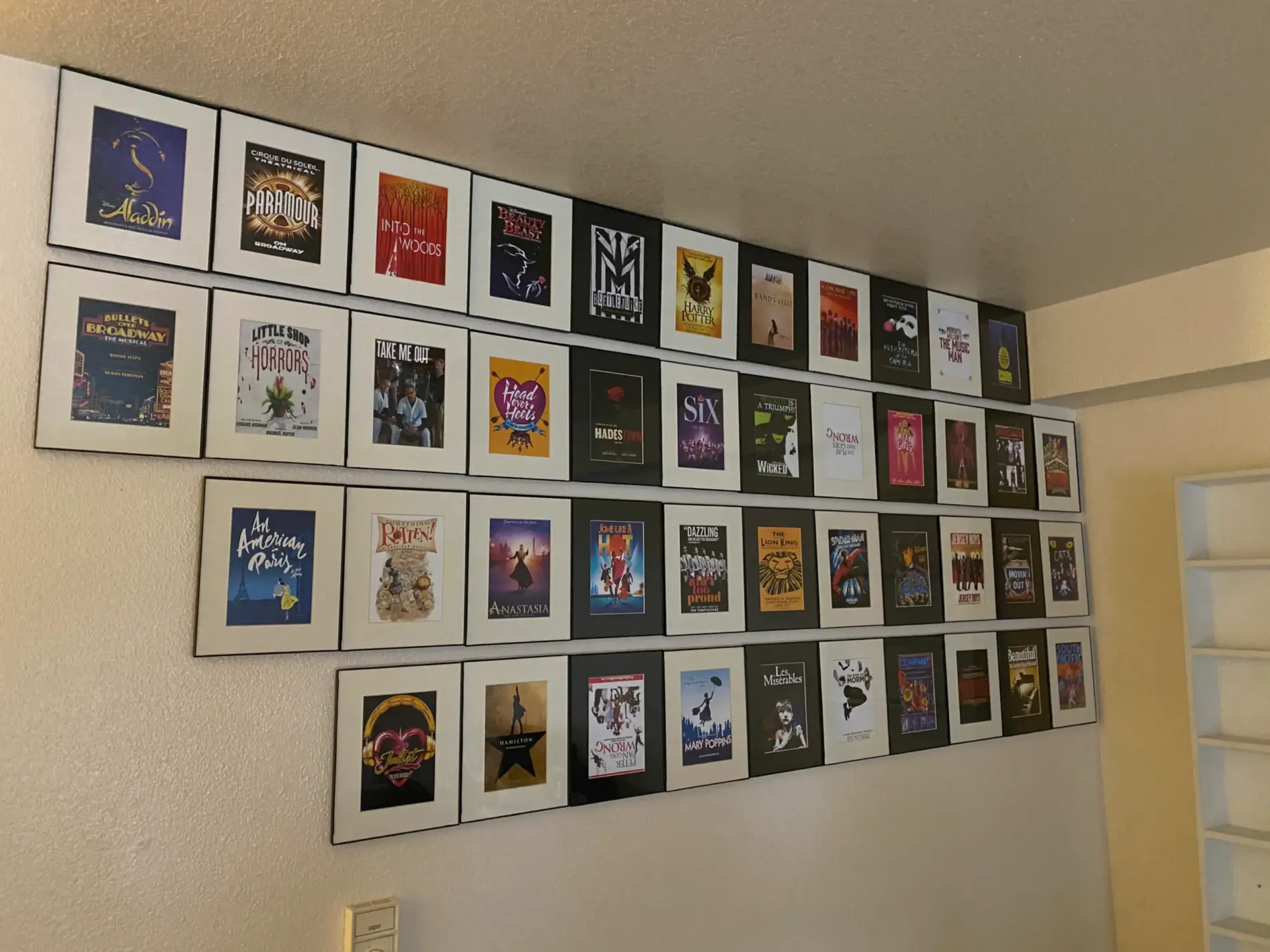 A wall covered edge-to-edge in framed Broadway show posters, including Hamilton, Wicked, and The Lion King