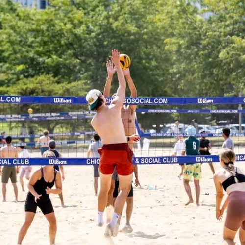 Dr. Ryan Smrz jumping to spike a volleyball at the net during an outdoor beach volleyball game