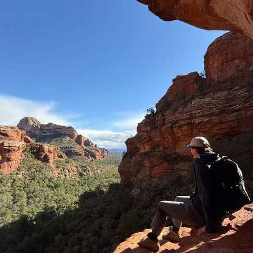 Dr. Ryan Smrz sitting on a red rock ledge taking in a canyon view while hiking